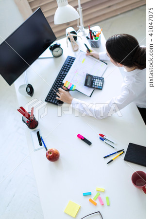 A young girl in the office sits at a table, holds a marker and a pencil in her hand and works with a 41047075