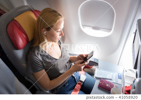 Woman listening to music on smart phone on commercial passengers airplane during flight. 41058920
