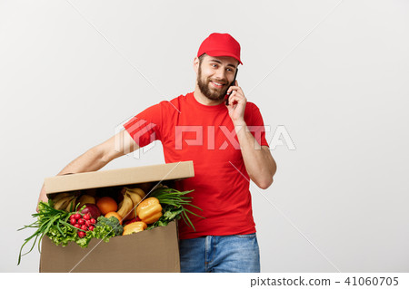 Delivery man holding paper box with food and making a call with mobile phone isolated over grey Delivery man holding paper box with food and making a call with mobile phone isolated over grey 41060705