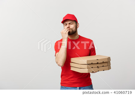 Delivery Concept: Handsome Pizza delivery man showing delicious expression over grey background Delivery Concept: Handsome Pizza delivery man showing delicious expression over grey background 41060719