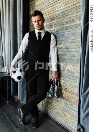 Stylish athletic man in a business suit and a soccer ball. Against the background of a loft wall. 41064423