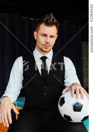 Stylish athletic man in a business suit and a soccer ball. Against the background of a loft wall. 41064426