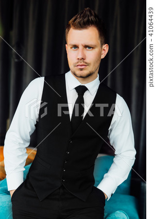 Stylish athletic man in a business costume vest. Sits in the turquoise sofa chair, a serious look. Stylish athletic man in a business costume vest. Sits in the turquoise sofa chair, a serious look. 41064439
