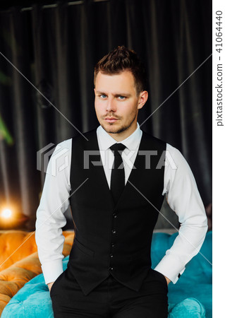 Stylish athletic man in a business costume vest. Sits in the turquoise sofa chair, a serious look. Stylish athletic man in a business costume vest. Sits in the turquoise sofa chair, a serious look. 41064440