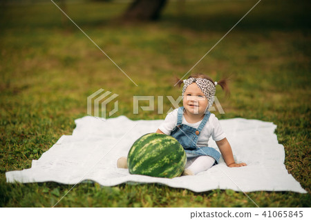 Little girl sitting in a park on plaid and eating a watermelon Little girl sitting in a park on plaid and eating a watermelon 41065845