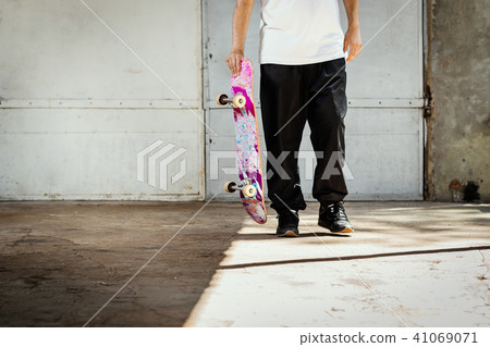 man holding a used skateboard in hand in a concrete skatepark 41069071