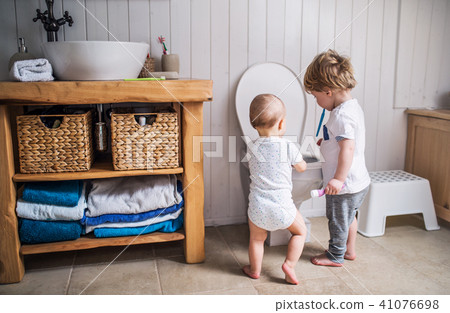 Two toddler children with toothbrush standing by the toilet in the bathroom at home. 41076698