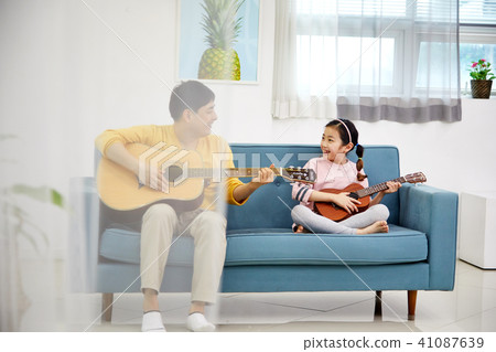 A happy family spending a holiday playing a guitar with a dad and a daughter on the living room sofa 41087639