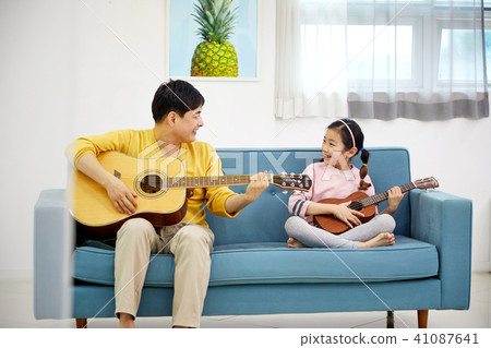 A happy family spending a holiday playing a guitar with a dad and a daughter on the living room sofa A happy family spending a holiday playing a guitar with a dad and a daughter on the living room sofa 41087641