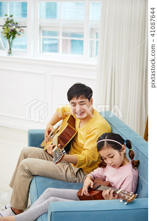 A happy family spending a holiday playing a guitar with a dad and a daughter on the living room sofa 41087644