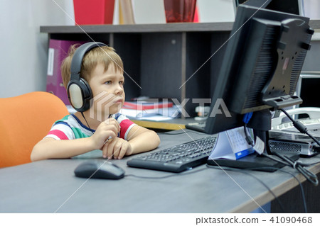 Little boy with headphones sitting at computer in office Little boy with headphones sitting at computer in office 41090468