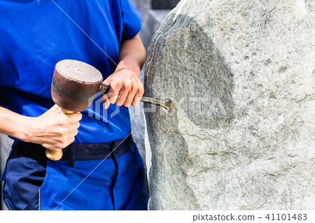 Stonemason working on boulder with sledgehammer and iron Stonemason working on boulder with sledgehammer and iron 41101483