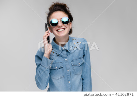 Young brunette girl in round glasses. Hairs are gathered in a bun. Girl with a black phone. The girl 41102971