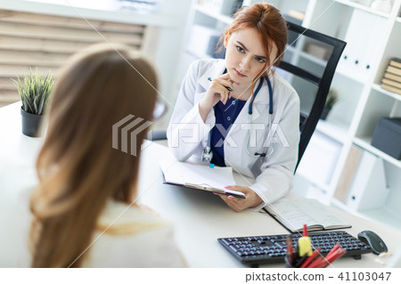A beautiful young girl in a white robe is sitting at the desk in the office and communicating with A beautiful young girl in a white robe is sitting at the desk in the office and communicating with 41103047