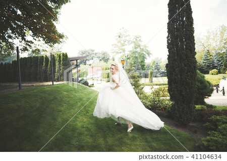 Beautiful bride in elegant white dress holding bouquet posing in park 41104634