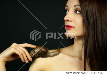 Portrait of Attractive Young Girl with Big Snail on Shoulder on Black Background in Studio 41107469