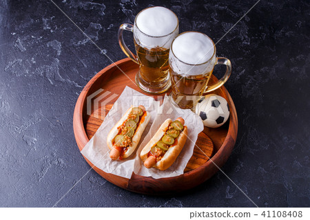 Photo on top of two glasses of beer and hot dogs on wooden tray with football Photo on top of two glasses of beer and hot dogs on wooden tray with football 41108408