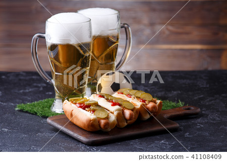 Photo of two mugs of foam beer, green grass with football, hotdogs Photo of two mugs of foam beer, green grass with football, hotdogs 41108409