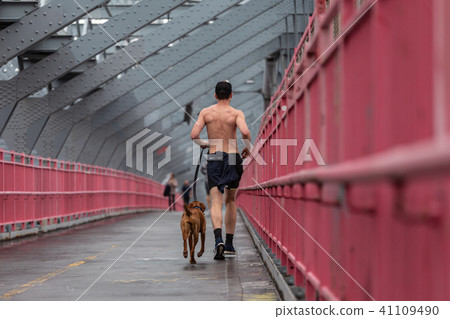 Unrecognizable topless recreational runner and a dog at Williamsburg bridgein New York CIty, USA. Unrecognizable topless recreational runner and a dog at Williamsburg bridgein New York CIty, USA. 41109490