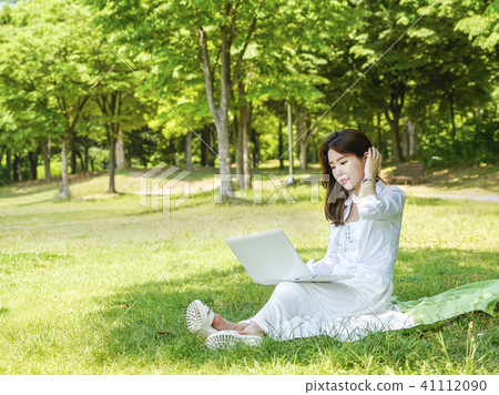 A young female model sitting on the lawn and looking at a laptop is holding one hand 41112090