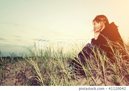 Sad young girl sitting alone on a grass outdoors, 41120042