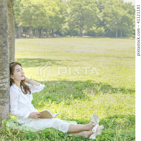 Young female model sitting on the lawn is leaning on the tree 41121181