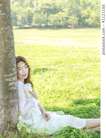 Young female model sitting on the lawn leaning on a tree 41121188