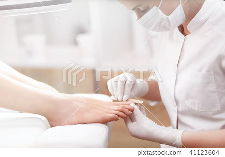 Nail artist in beauty salon polish nails on foot by tool. Nail artist in beauty salon polish nails on foot by tool. 41123604