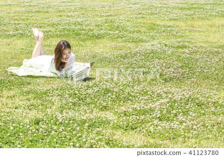 Young female model sitting down on the lawn and looking at the book 41123780