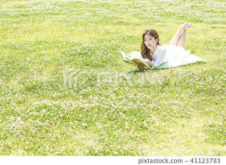 Young female model sitting down on the lawn and looking at the book 41123783