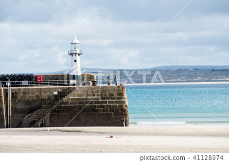 A small lighthouse and a tourist who stands at the end of the breakwater at the entrance of the tide where the tide has drawn 41128974