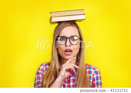 young woman in glasses holding books on her head. Smiling young stylish student is standing with 41131731