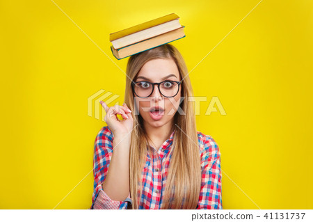 young woman in glasses holding books on her head. Smiling young stylish student is standing with 41131737