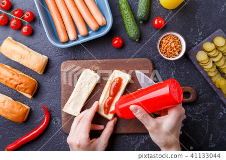 Picture on top of table with ingredients for hot dogs, cutting board, man's hands 41133044