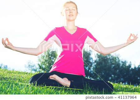 Female 26-32 years old in pink T-shirt is sitting and meditating Female 26-32 years old in pink T-shirt is sitting and meditating 41137964