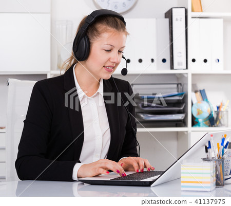 Young woman in black suit is talking by headset with client Young woman in black suit is talking by headset with client 41137975