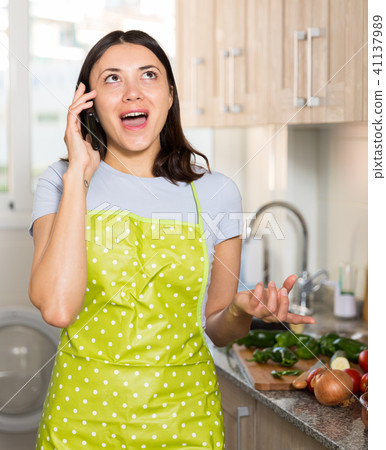 Girl housewife in apron talking by phone at home kitchen 41137989