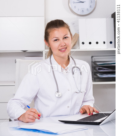 Doctor girl in uniform is working behind laptop with documents Doctor girl in uniform is working behind laptop with documents 41138111