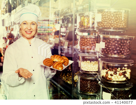 Elderly smiling seller with dark and white chocolates 41140077