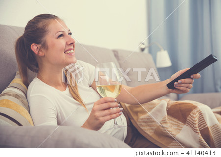 Young female is watching TV and sitting with white wine Young female is watching TV and sitting with white wine 41140413