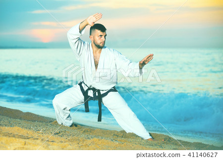 Man in uniform doing taekwondo exercises at sunset sea shore Man in uniform doing taekwondo exercises at sunset sea shore 41140627