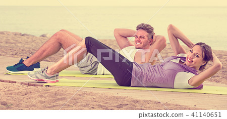 Young woman and guy training on beach by ocean Young woman and guy training on beach by ocean 41140651