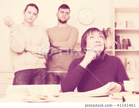 Upset elderly mother with documents, dissatisfied children behind Upset elderly mother with documents, dissatisfied children behind 41141461