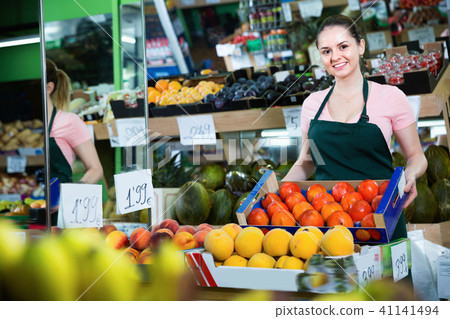 Young smiling saleswoman with box of ripe orange persimmons in store Young smiling saleswoman with box of ripe orange persimmons in store 41141494