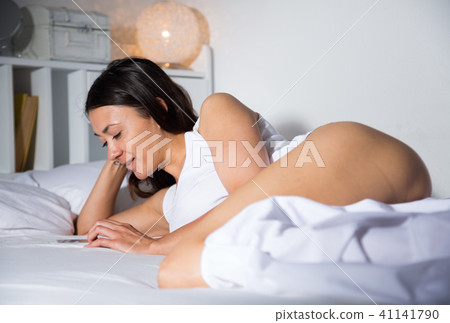 Young sexy girl lying and using smartphone on white sheet in bed Young sexy girl lying and using smartphone on white sheet in bed 41141790