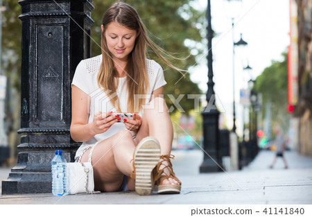 Girl using phone while relaxing near lamp post Girl using phone while relaxing near lamp post 41141840