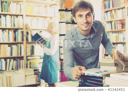 Young glad man choosing new book from many 41142451