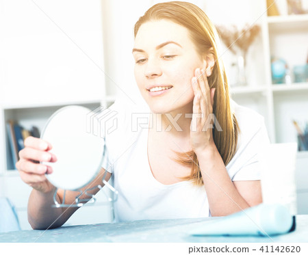 Smiling female is looking on her skin in the mirror 41142620