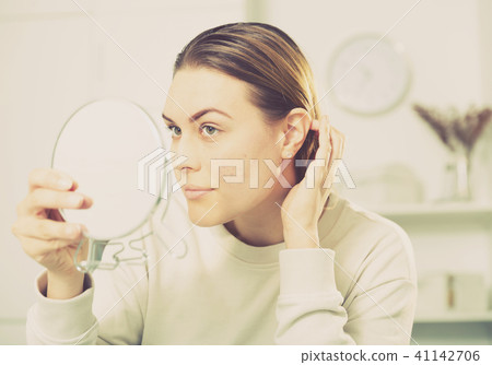 Cheerful woman is concentrared looking on her face in the mirror 41142706