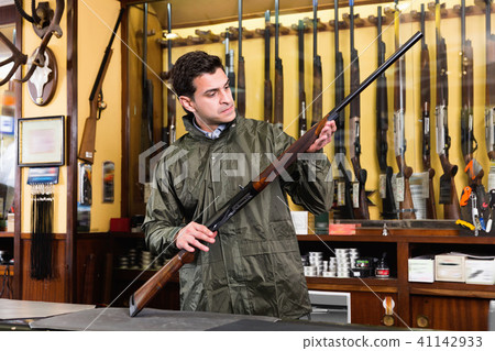 Confident hunter male wearing windbreaker in hunting shop with r Confident hunter male wearing windbreaker in hunting shop with r 41142933